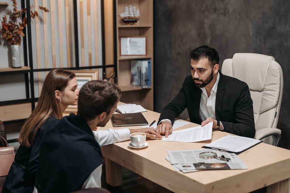 A professional florist specialist from flowersneweltham.co.uk is engaged in a detailed consultation with two clients in an office setting. The florist, a man with dark hair and a neatly trimmed beard,